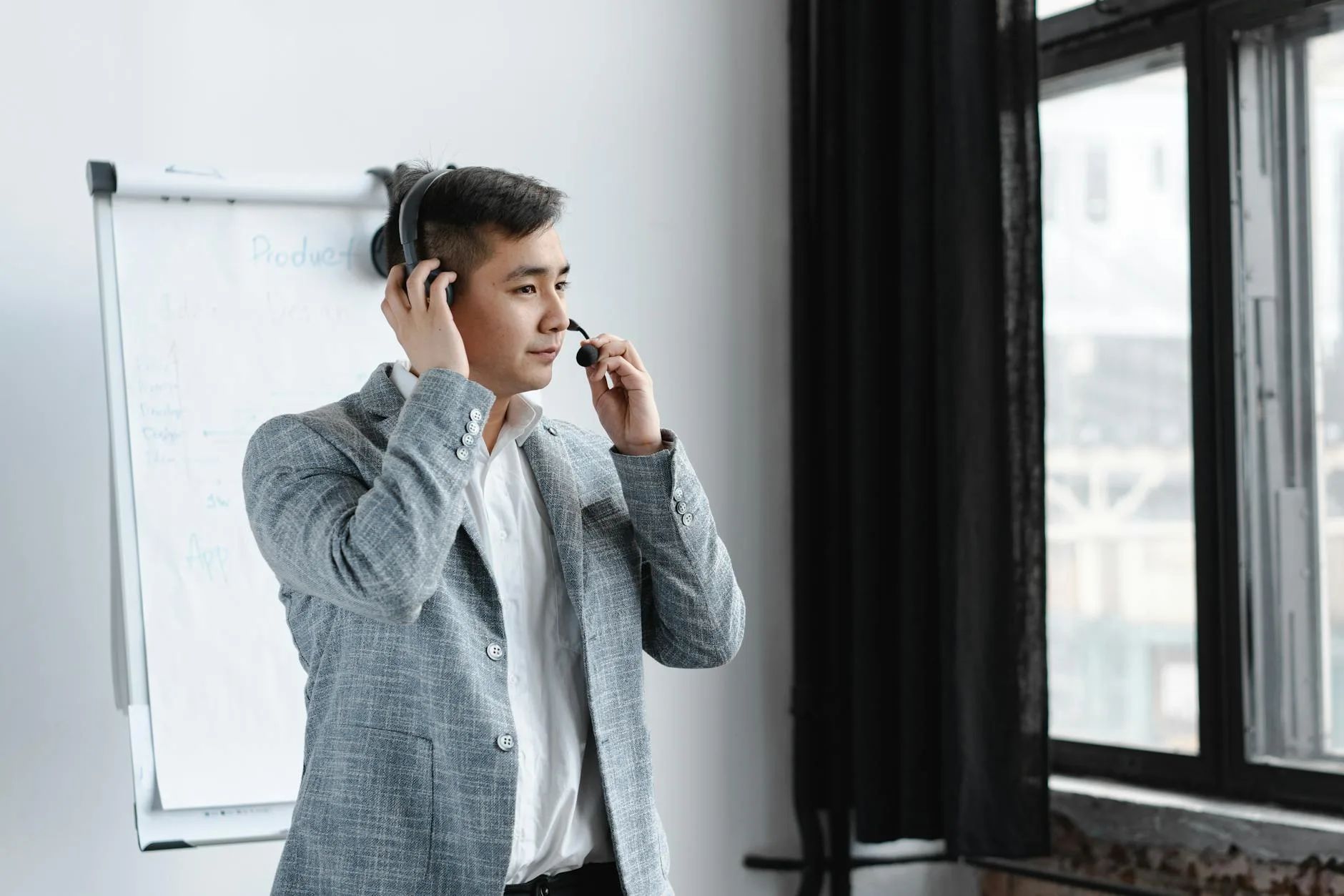 [Pexels] Asian call center agent wearing a headset, handling customer service at an office with a window view.