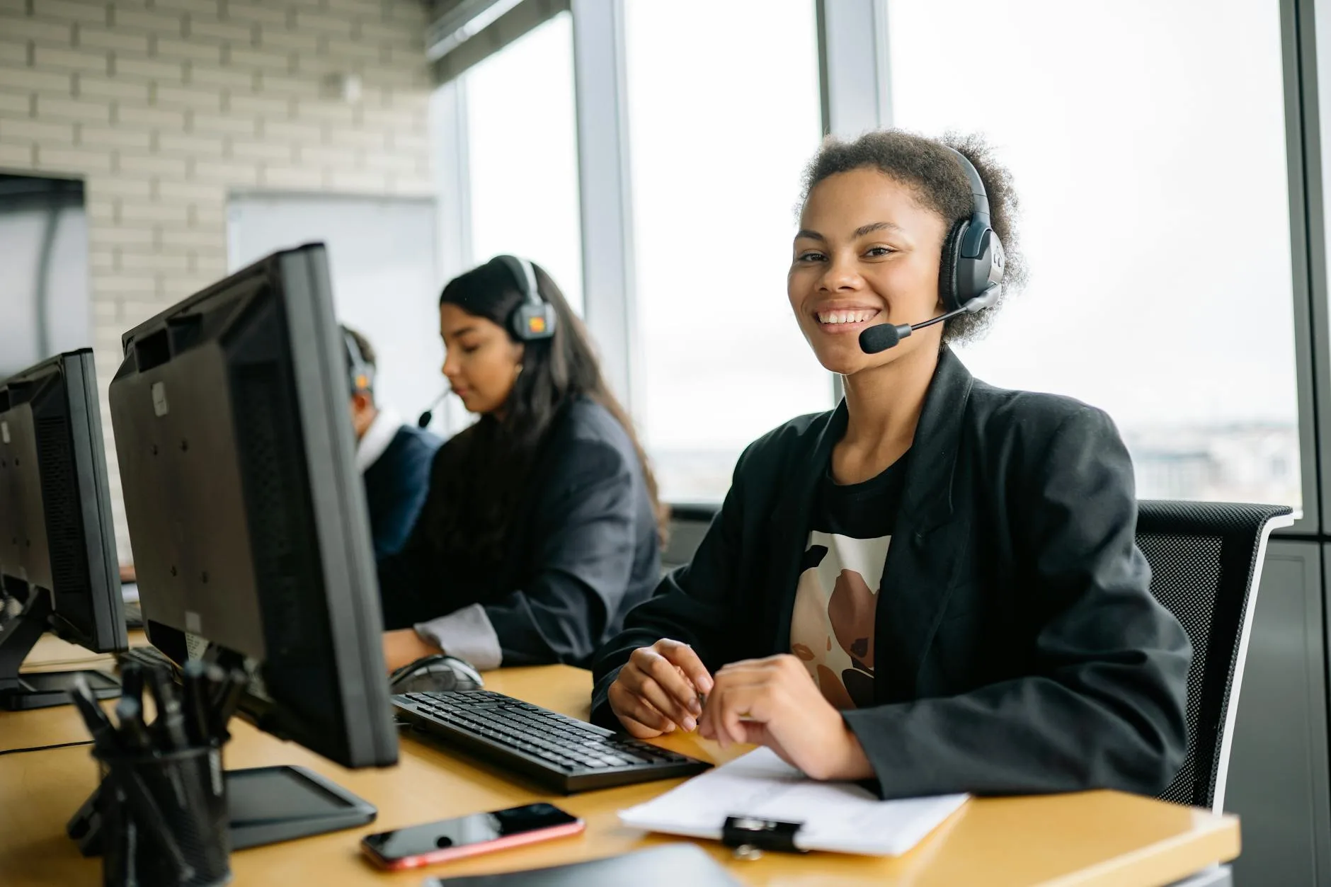 Smiling customer service representatives with headsets working in a bright modern office.