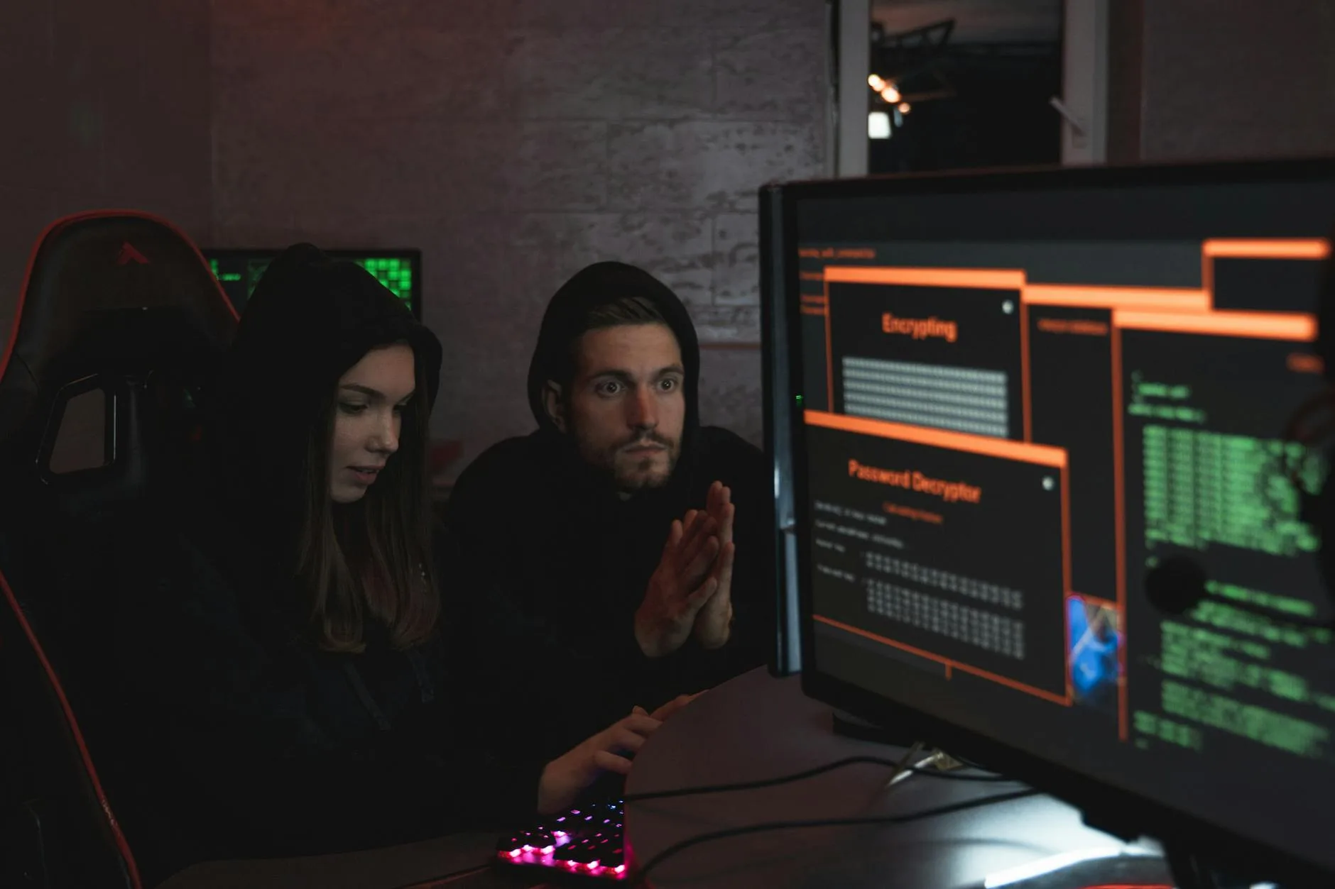 Cybersecurity experts in hoodies analyzing encrypted data on computer screens in an indoor setting.