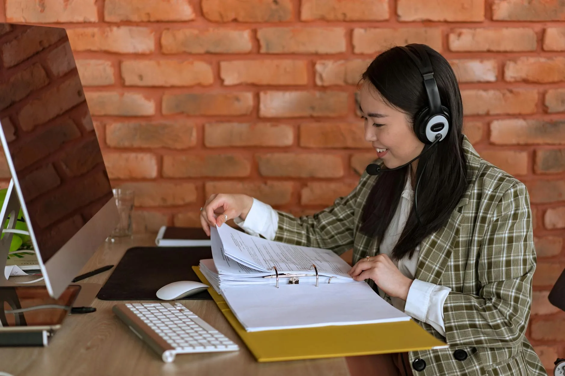 Smiling support agent with a headset and files at her workspace, engaging in a professional environment.