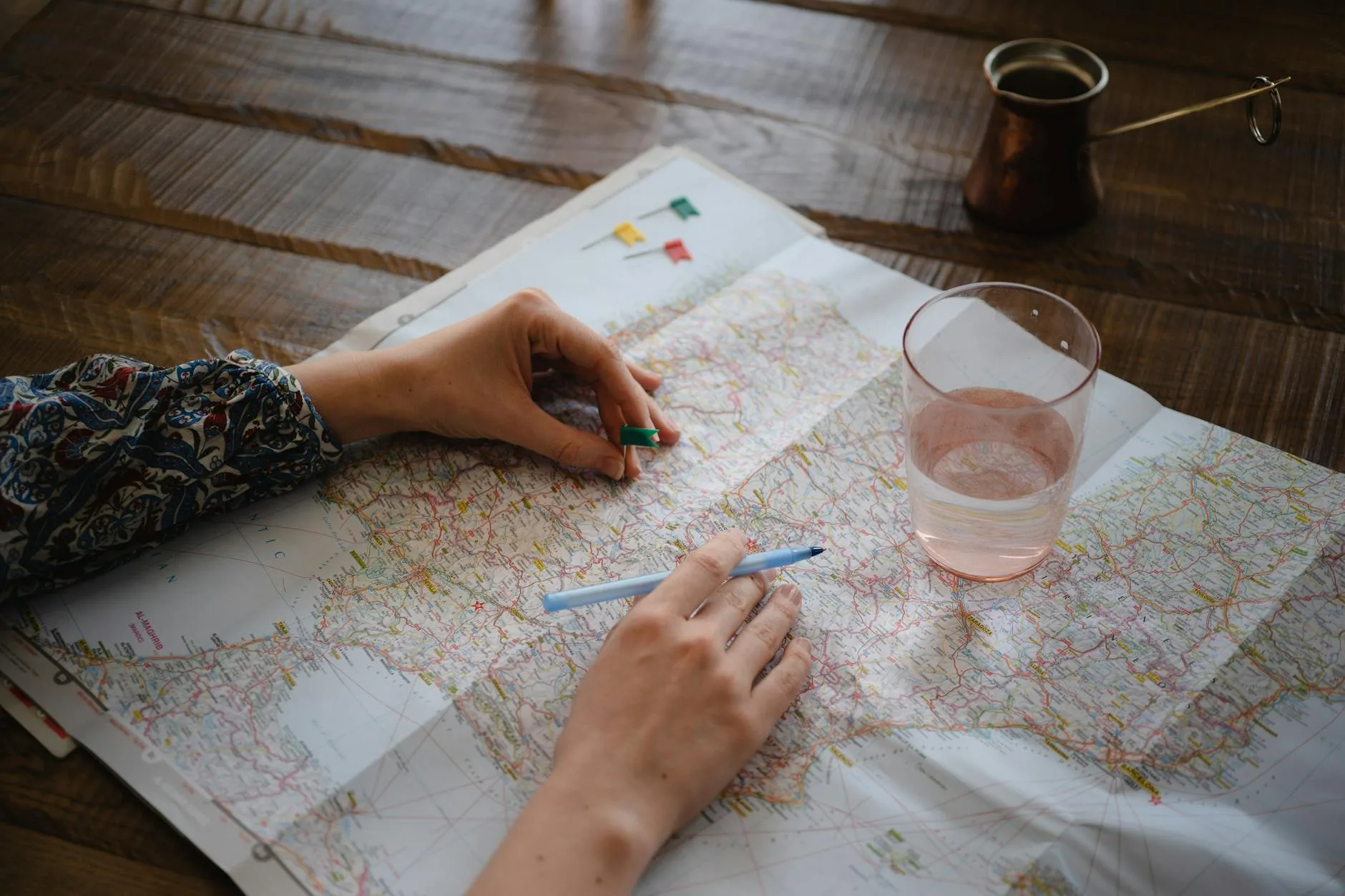 A woman places a pin on a map while planning a trip, with a glass of water nearby.