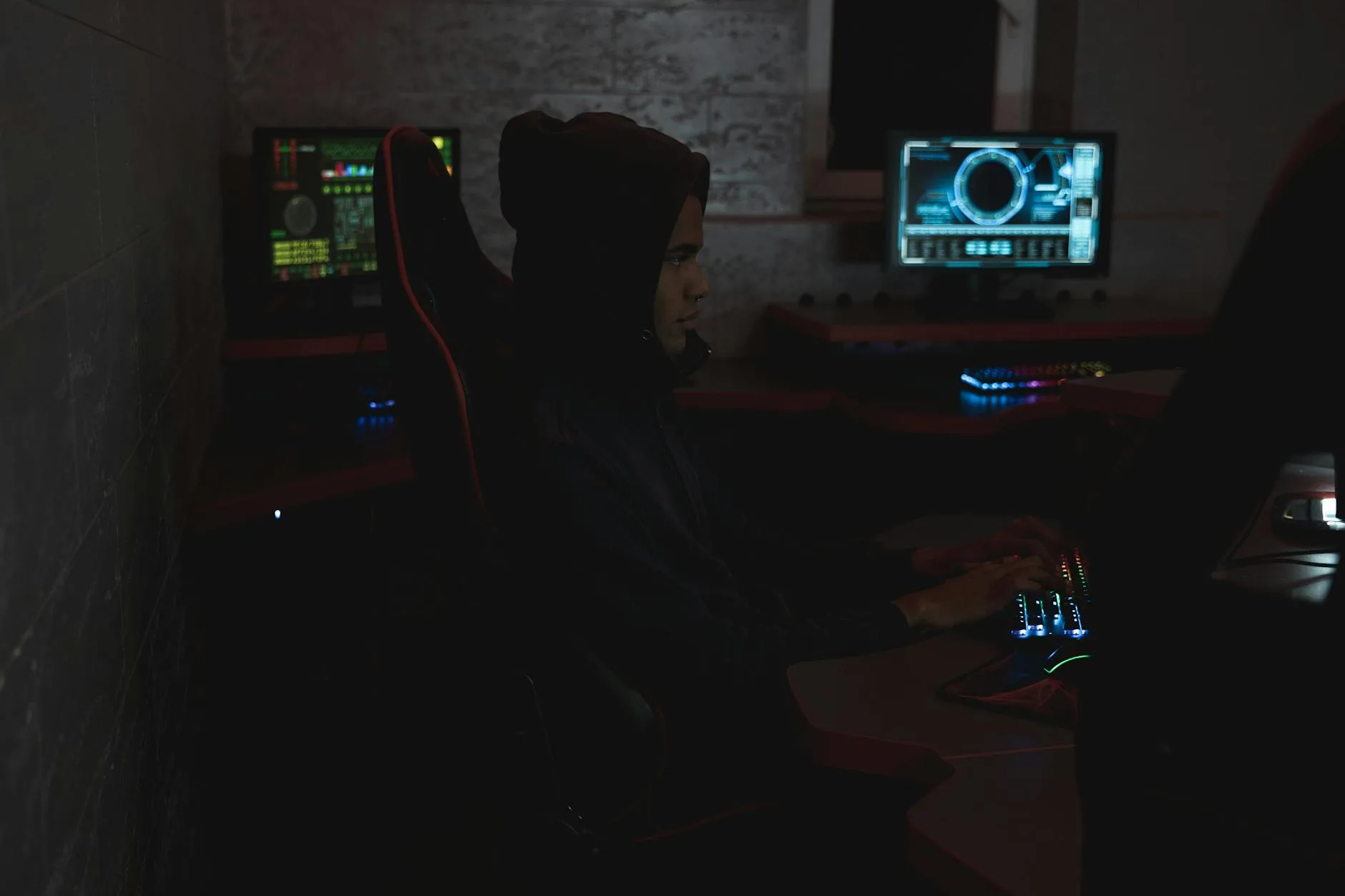 A professional analyzing data on multiple monitors in a dark room, highlighting cybersecurity themes.