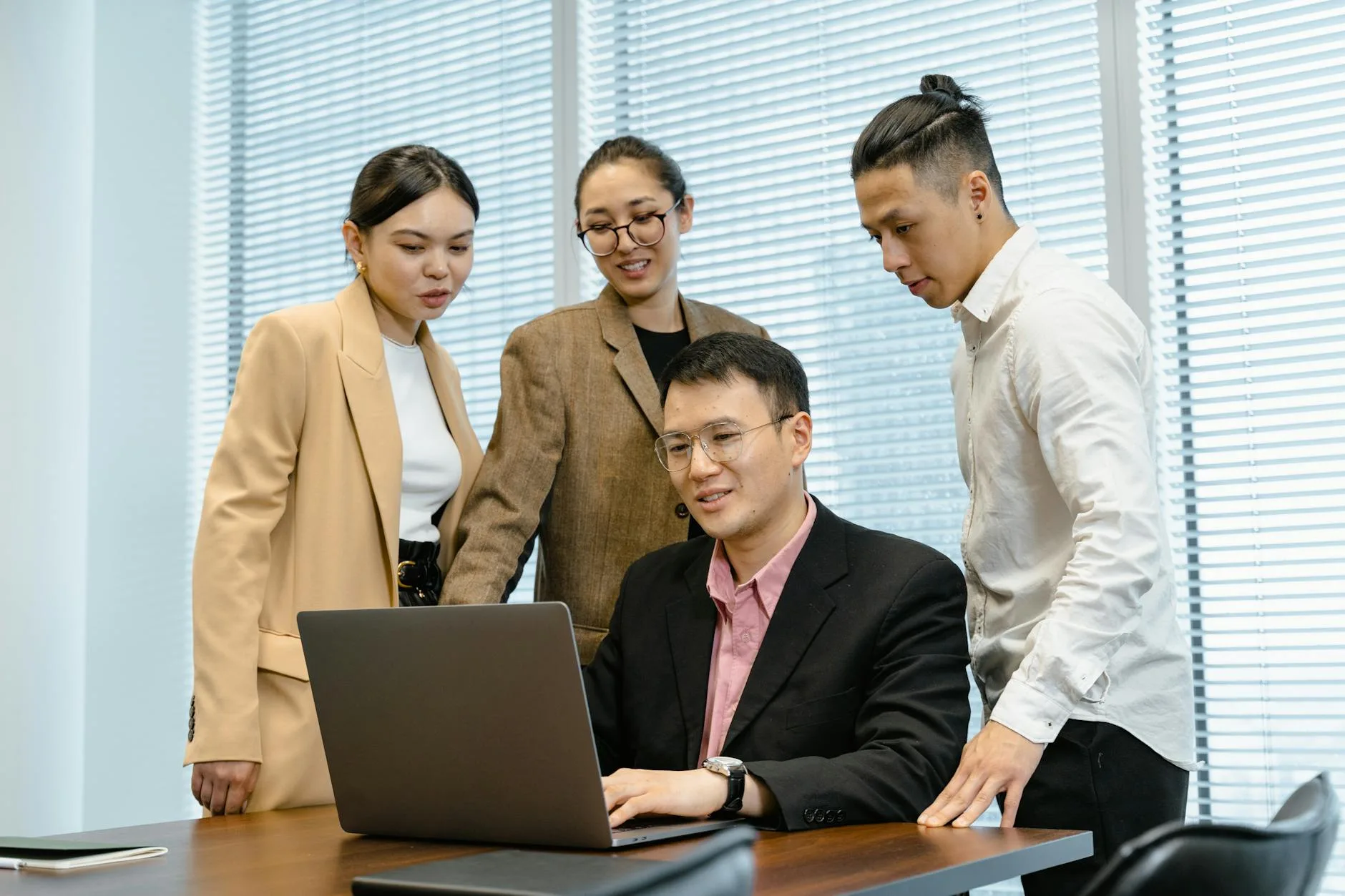 Four colleagues engaged in a discussion around a laptop during a business meeting.