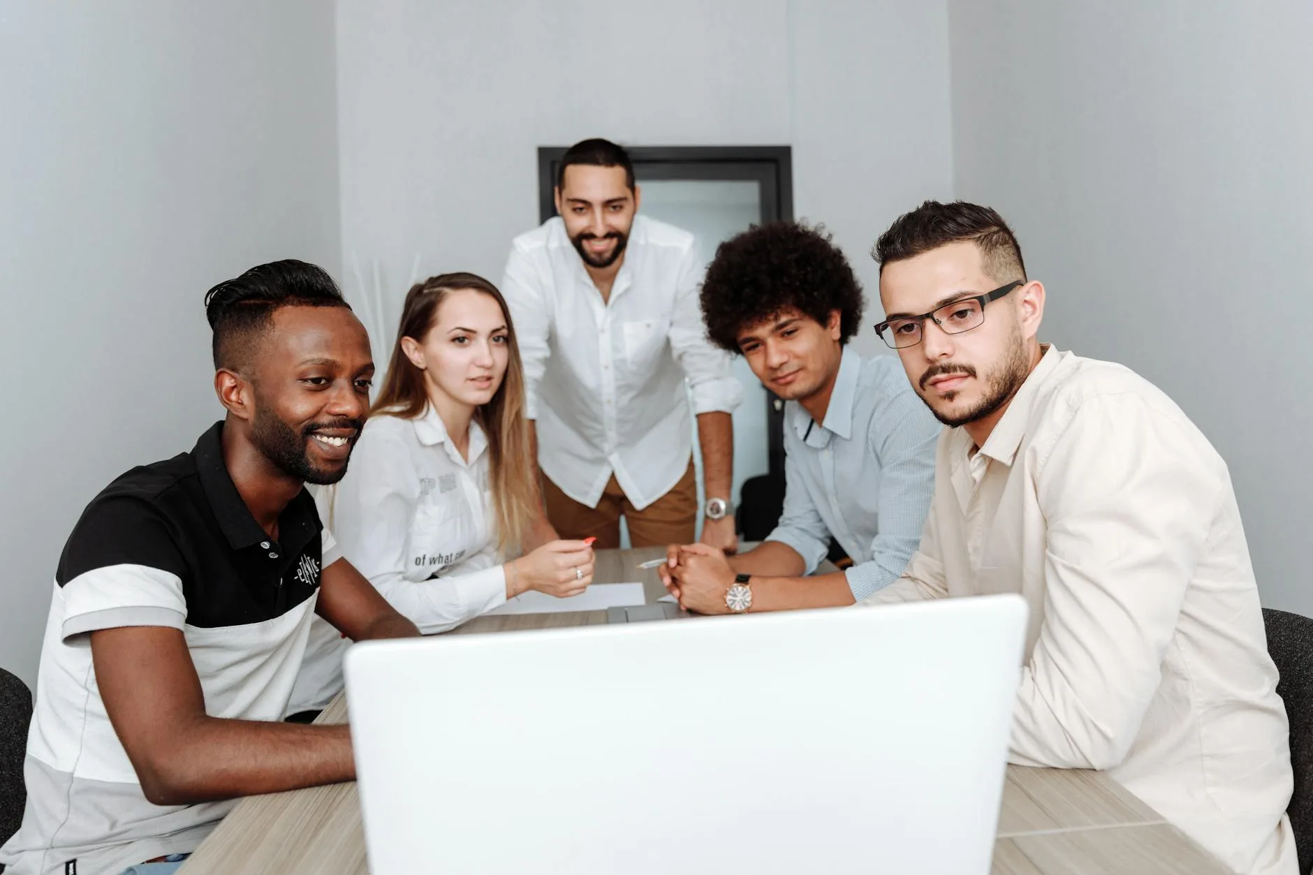 A diverse group of professionals engaging in a collaborative meeting around a laptop in an office.