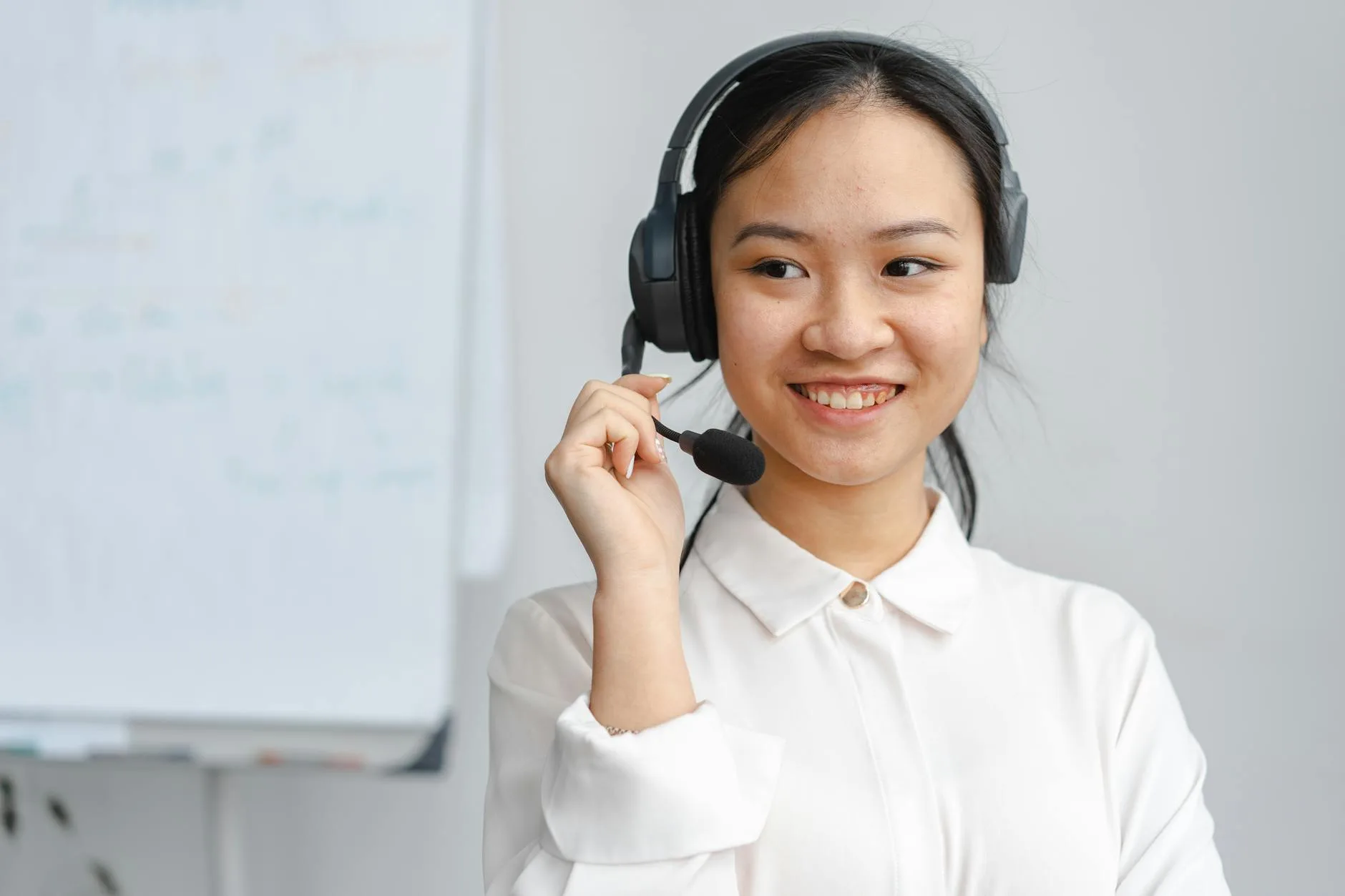 Asian woman smiling in a customer service role wearing a headset indoors.
