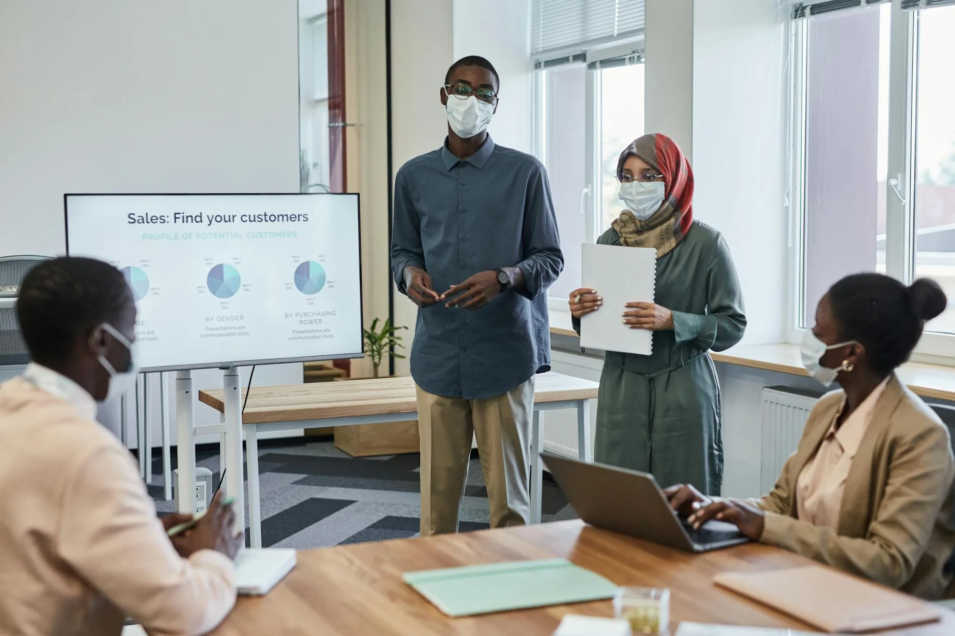 Business team presenting sales data while wearing face masks in a modern office.