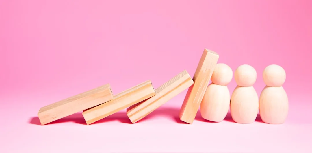 Wooden blocks falling towards small figures on pink background