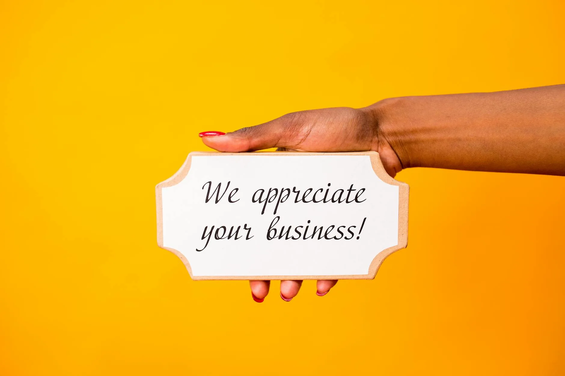 A hand holding a thank you sign with 'We appreciate your business!' on a vibrant yellow background.