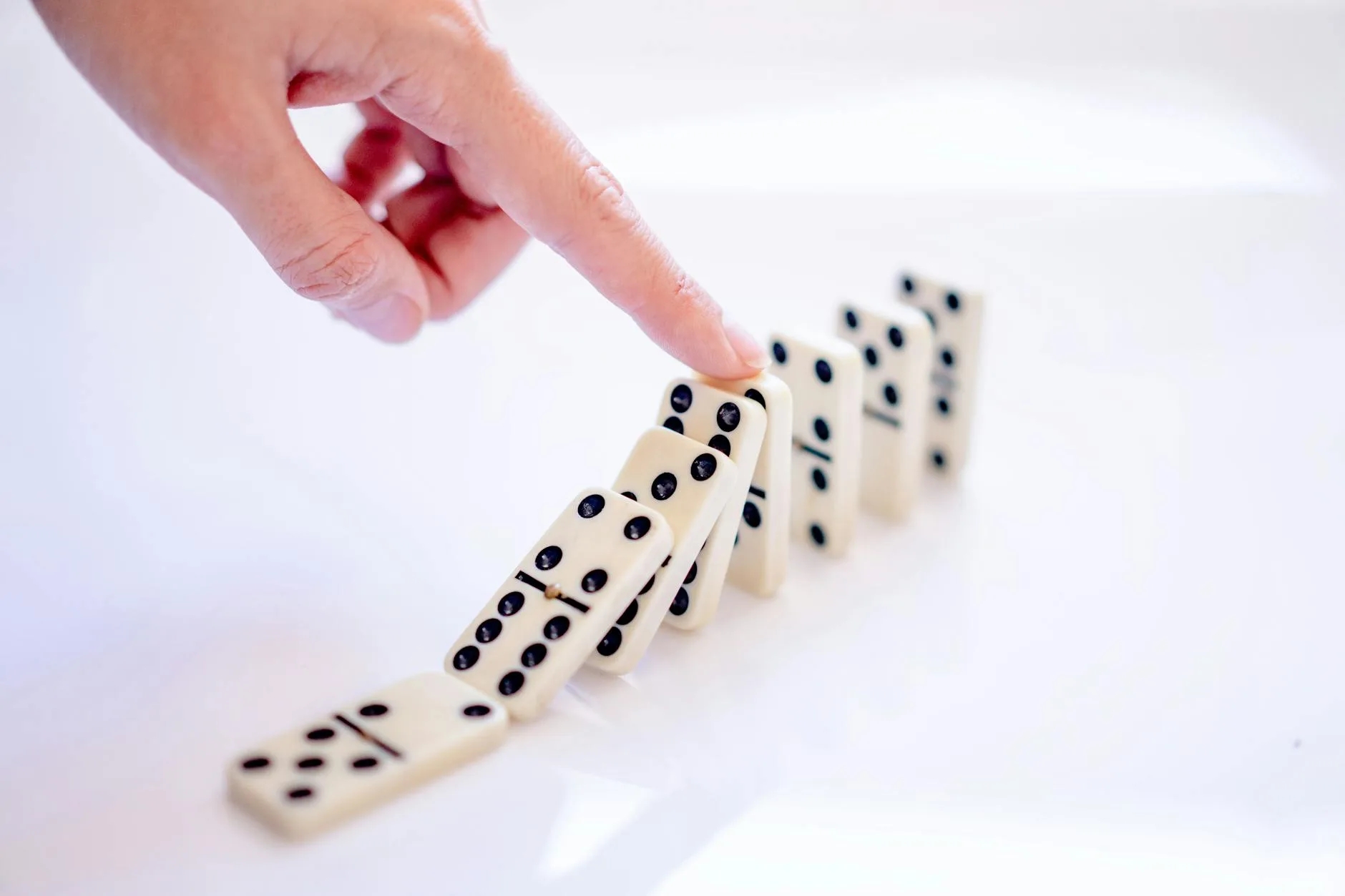 A close-up shot of a hand pushing dominoes, illustrating cause and effect.