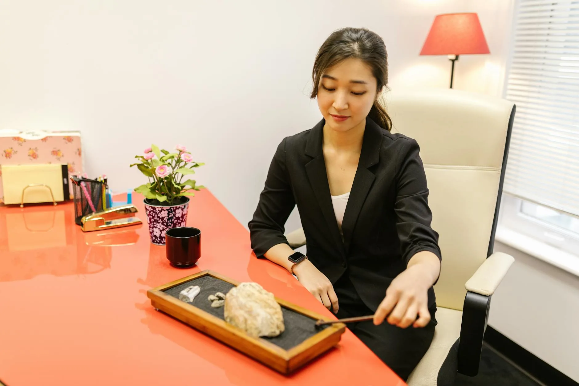 Asian businesswoman practicing stress relief at work with a zen garden indoors.