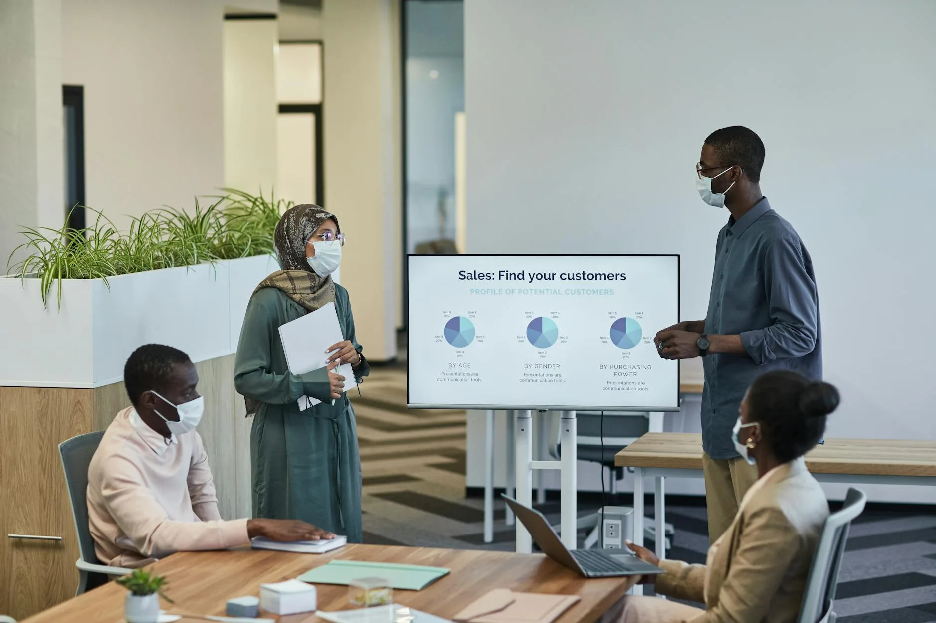 Business professionals in masks discuss customer profiles in a modern office setting.