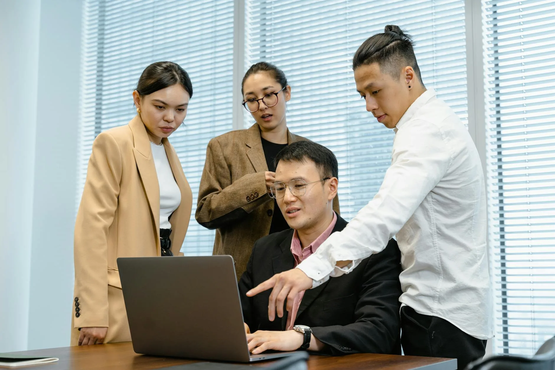 A group of professionals engage in teamwork around a laptop in a modern office setting.