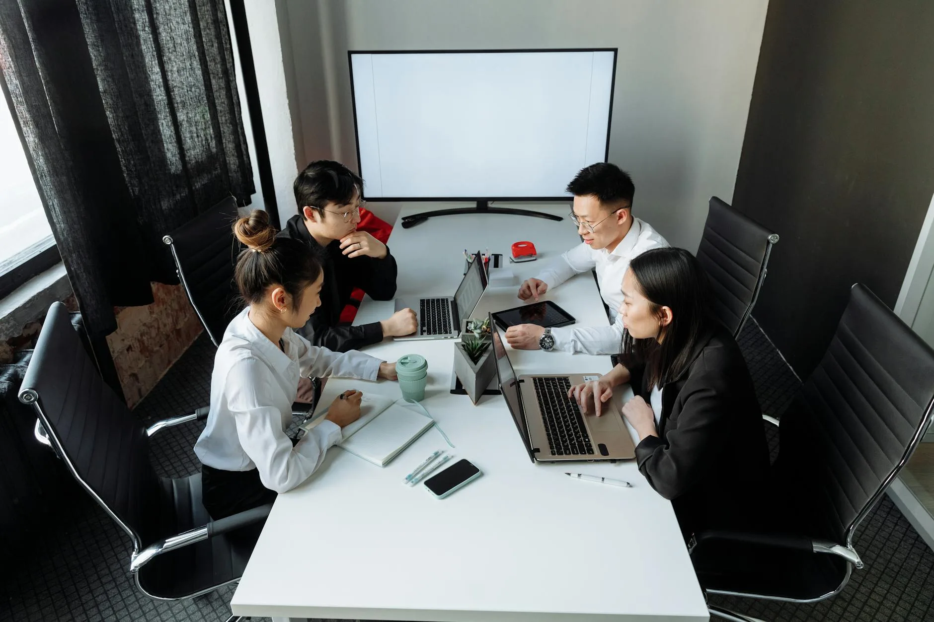 Four professionals collaborating over laptops in a bright, modern office space.