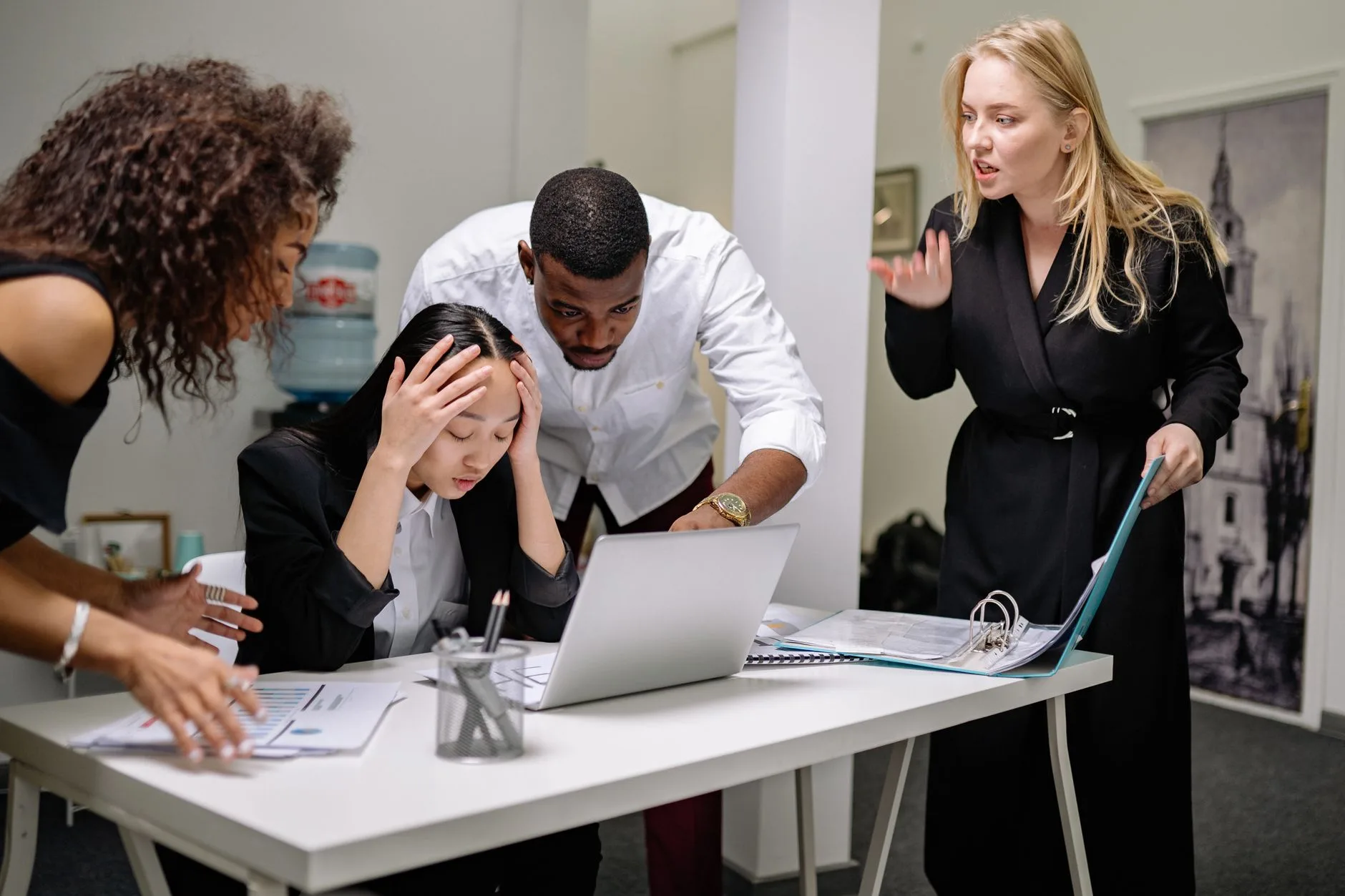 Group of diverse colleagues in an office engaged in a heated discussion around a laptop.