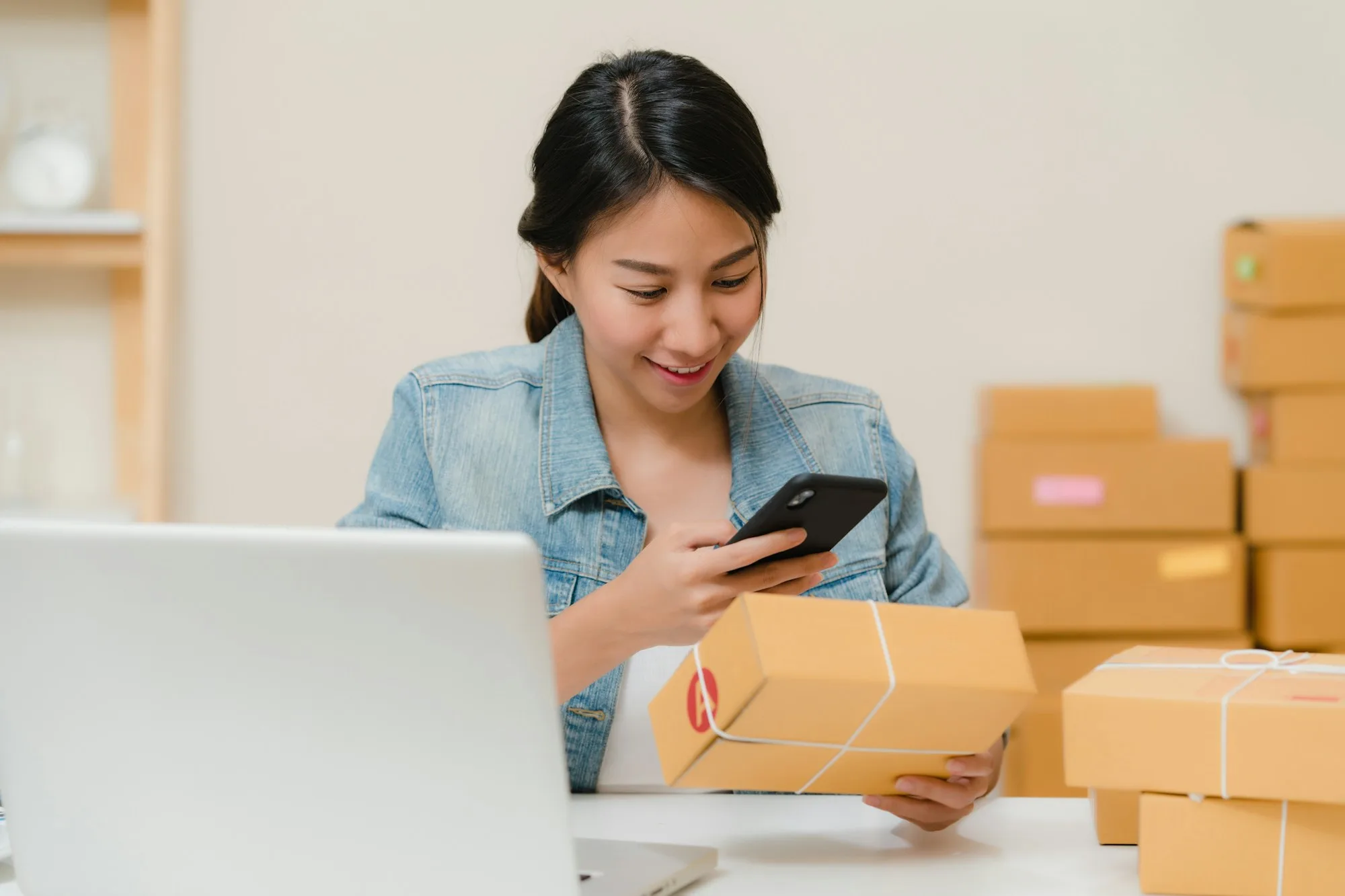 Chủ shop online kiểm tra đơn trên điện thoại bên các hộp hàng, khách hàng mà doanh nghiệp giao hàng chặng cuối cần giữ chân