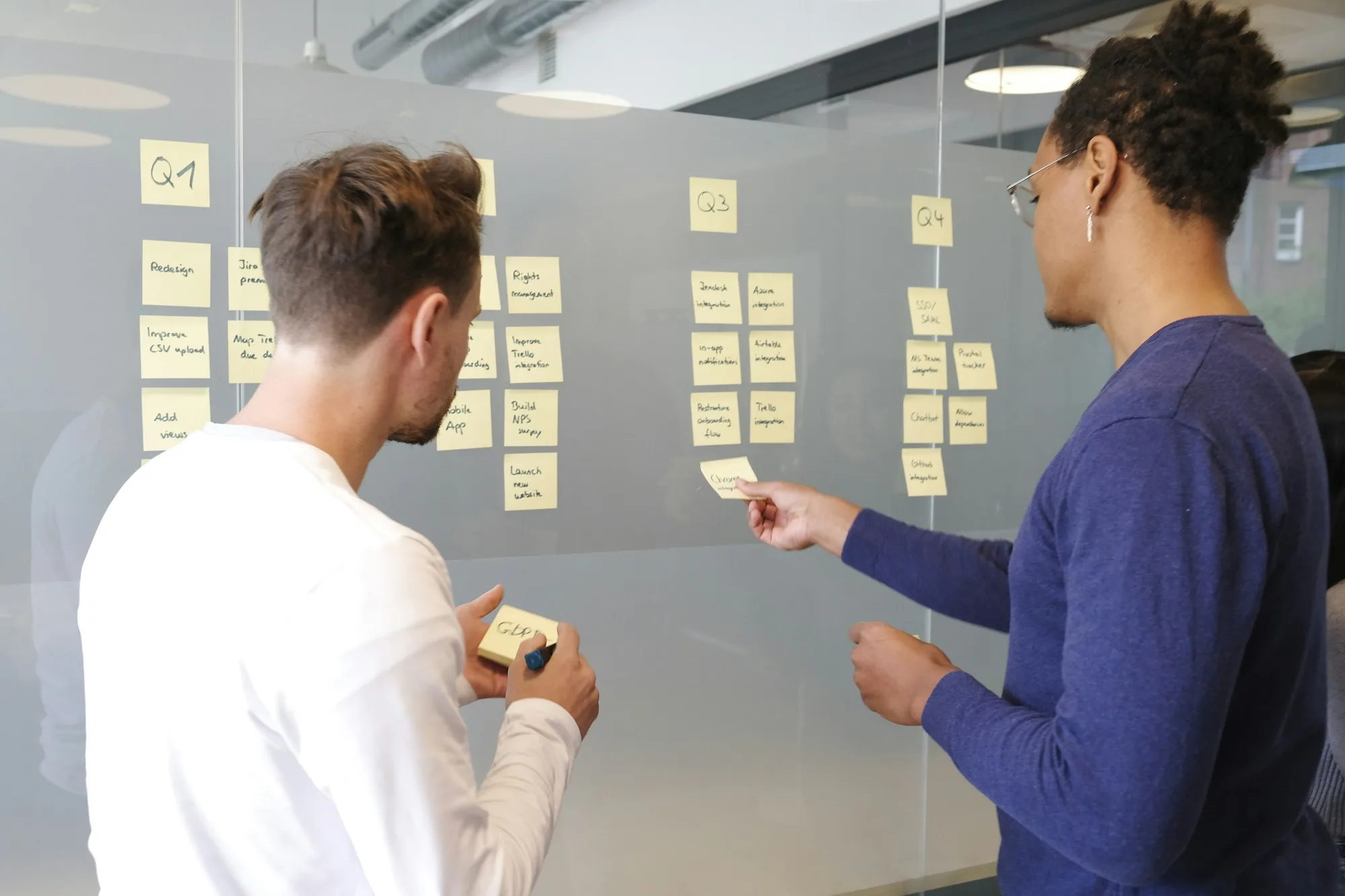 Hai nhân viên sắp xếp công việc trên bảng kanban giấy, cách làm trước khi chuyển sang công cụ quản lý dự án miễn phí